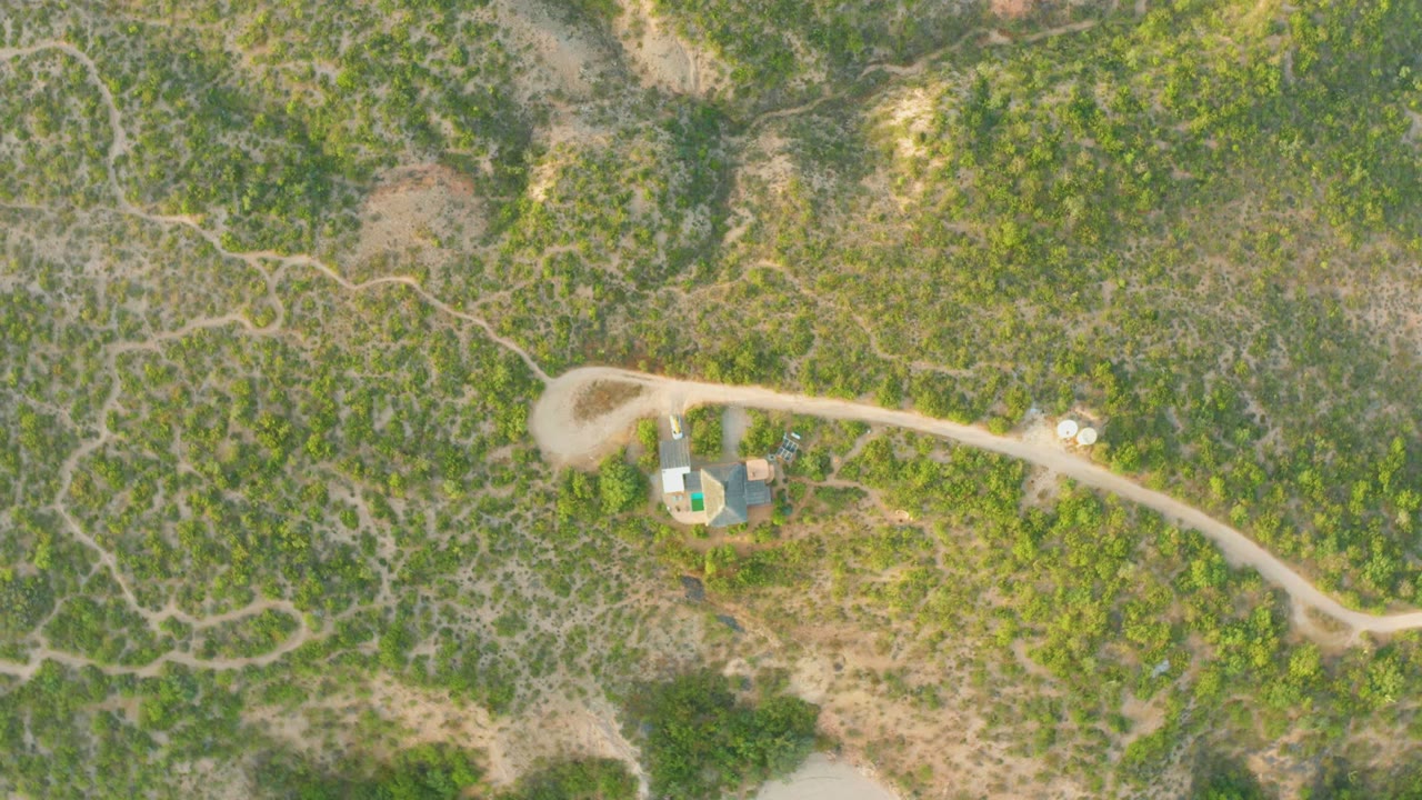 Overhead Cabo Pulmo aerial view with a pale road, low scrub, branching footpaths, and small built structures near the road, with no visible people.