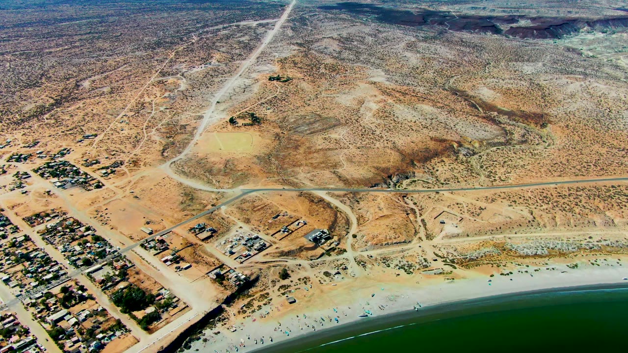 Drone view of beach, desert roads, settlement, and inland scrub.