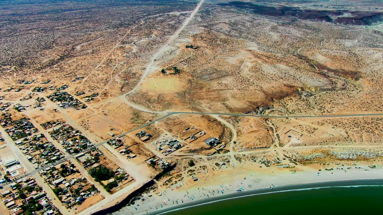 Drone view of sandy beach below a desert residential area.