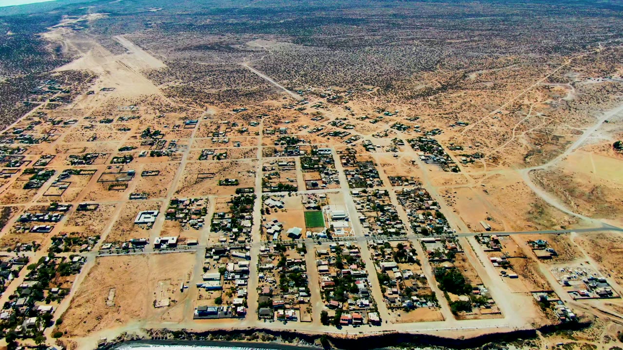 Aerial town blocks and pale roads with desert terrain beyond.