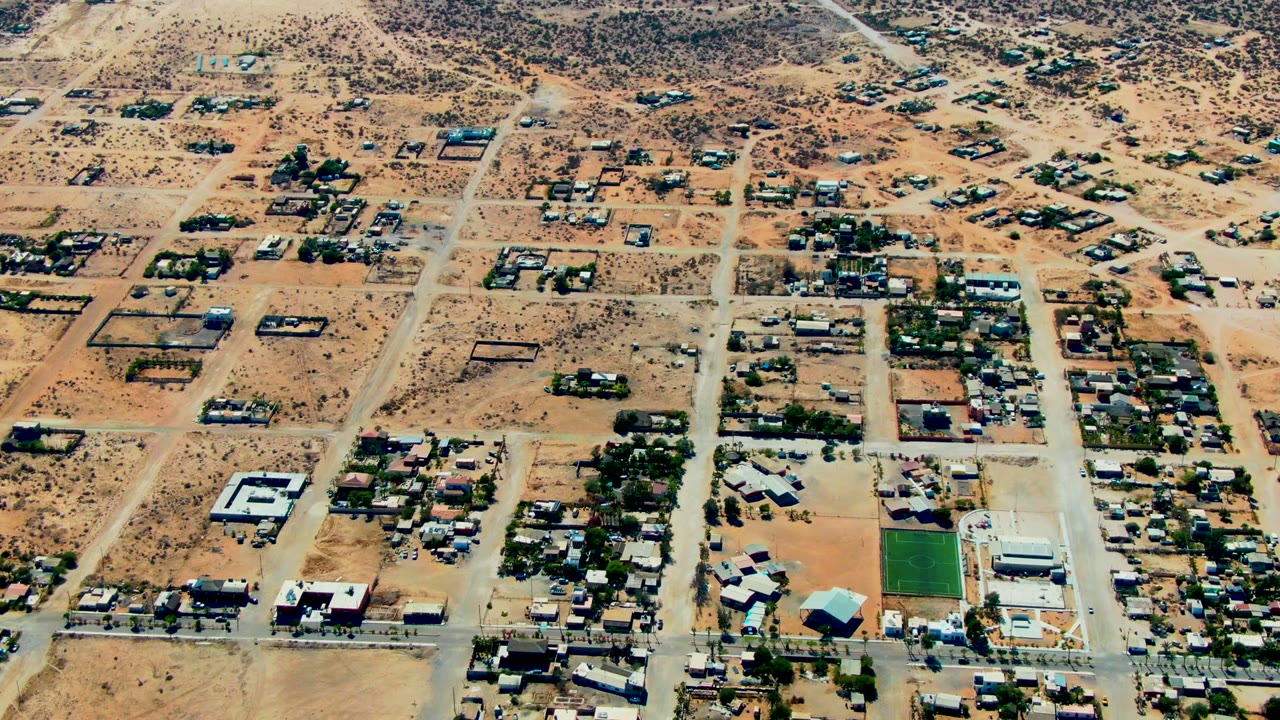 High aerial view over San Juanico, Baja California Sur showing sandy grid roads, scattered homes, sparse desert shrubs, and no visible people.