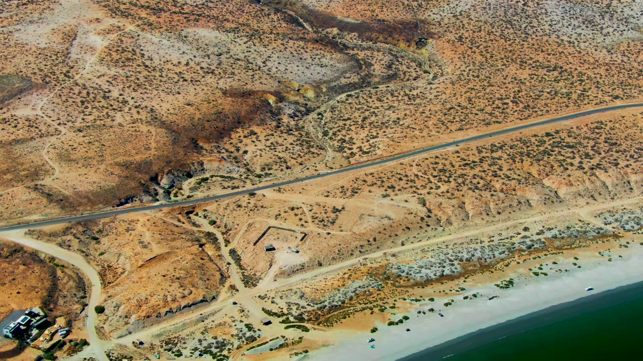 Overhead desert coastline with road, beach, and sparse structures