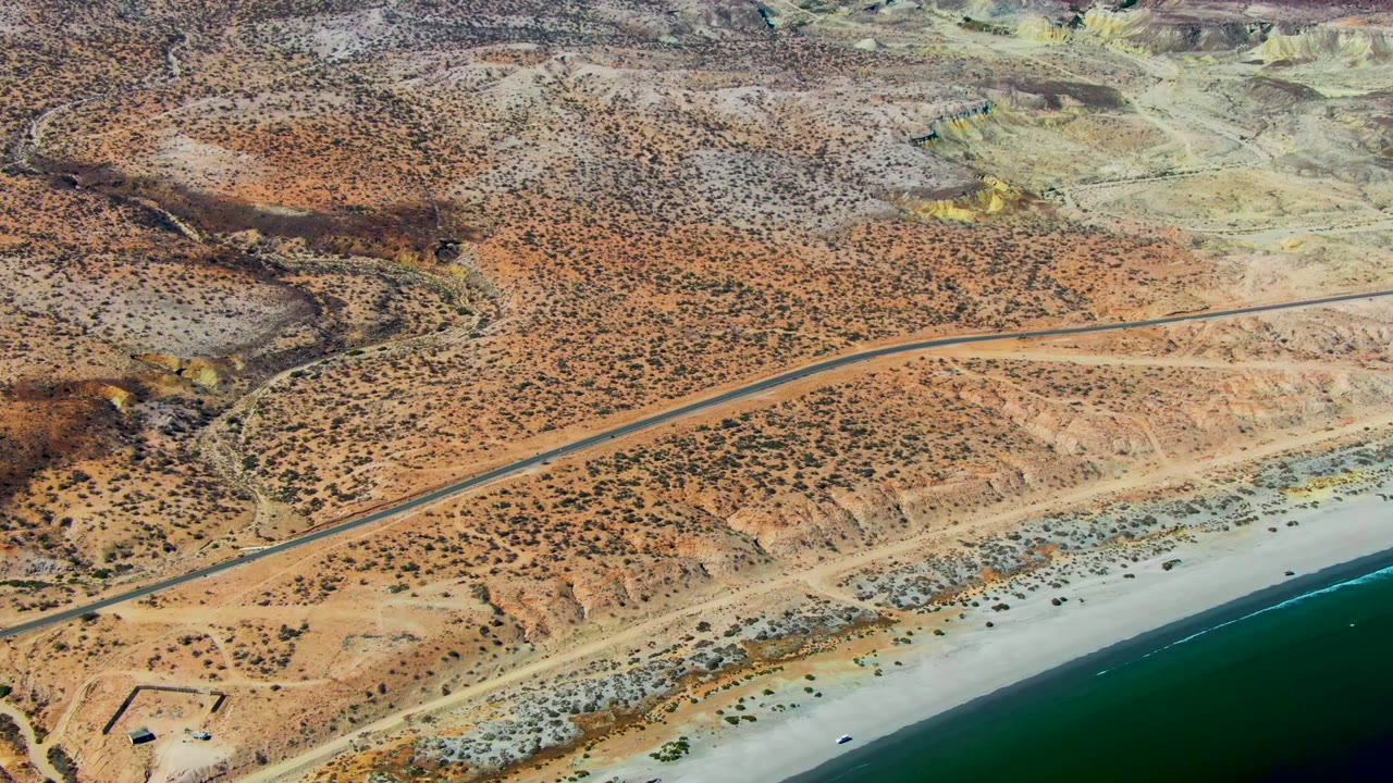 Aerial road crossing dry hills above a beach and ocean.