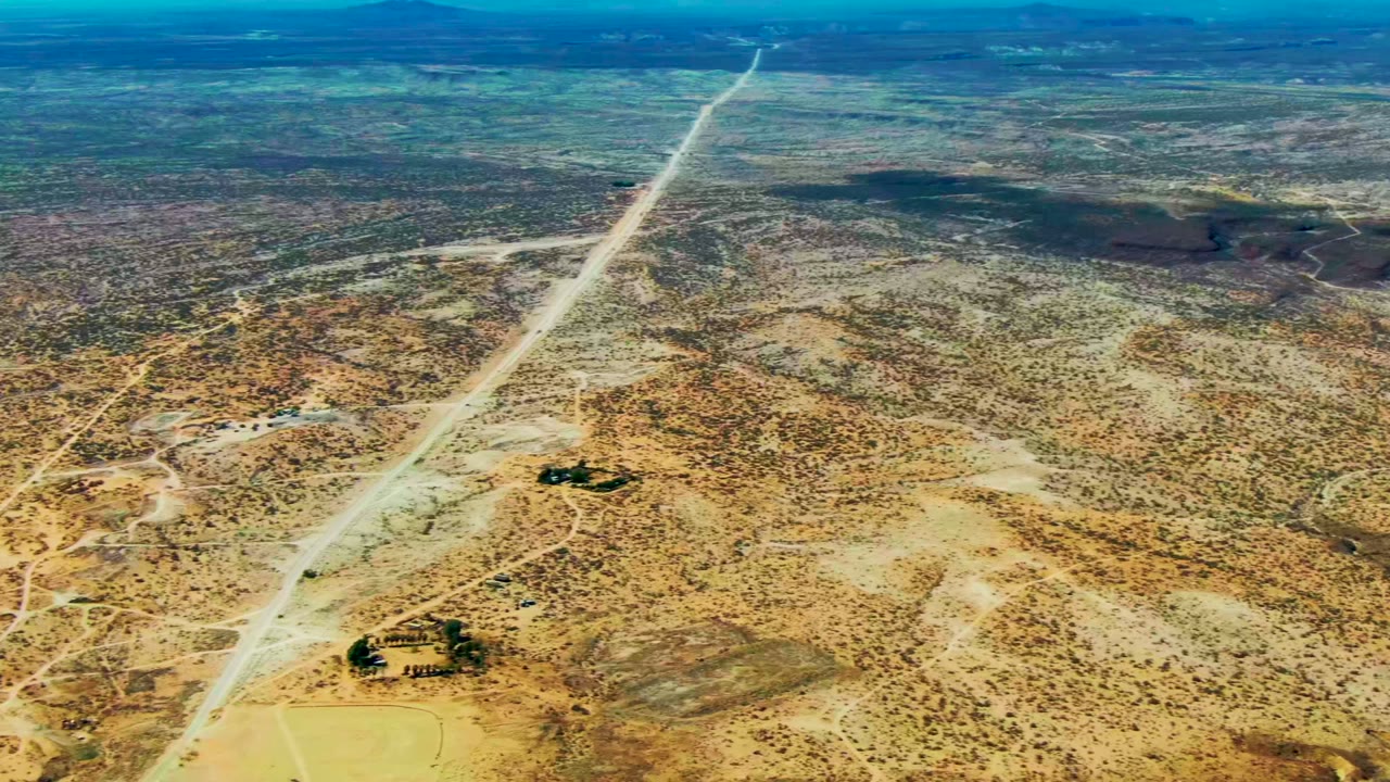 Aerial view of a long dirt road crossing sparse desert.