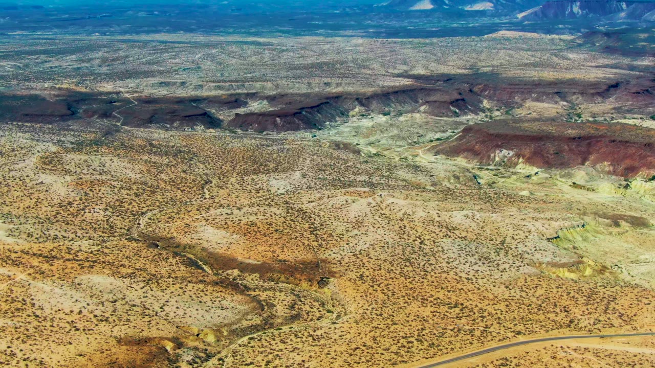Wide aerial desert landscape with reddish hills and sparse vegetation.