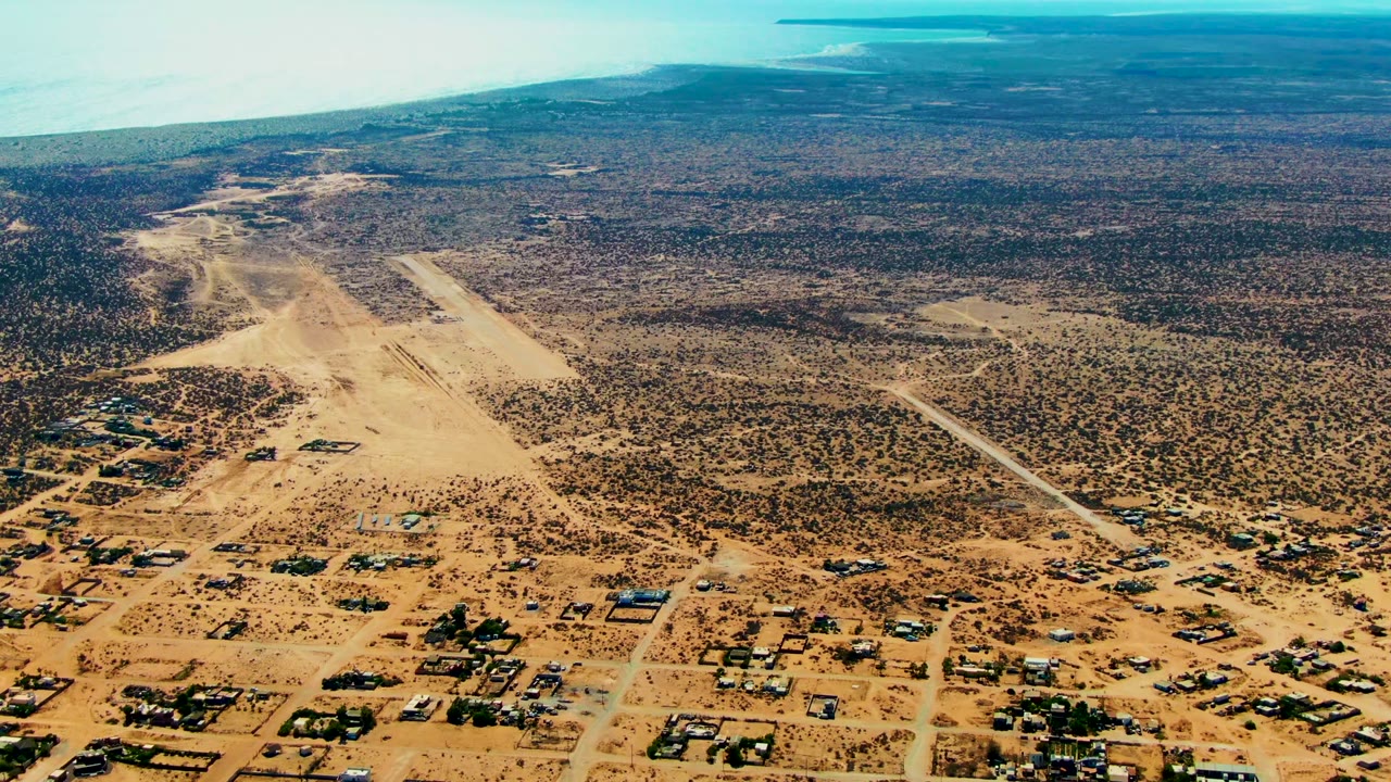 Aerial view over San Juanico, Baja California Sur showing dry scrubland, scattered structures, dirt roads, and runway-like clearings, with no visible people.