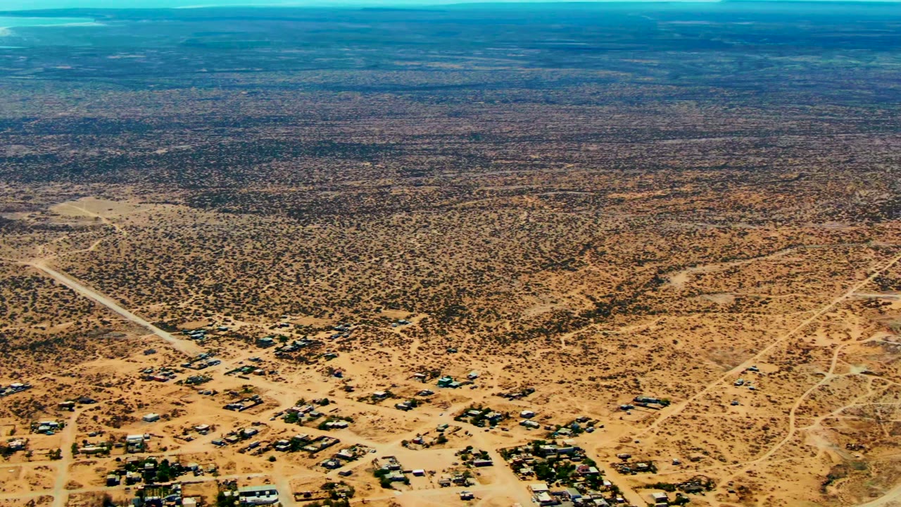 Wide aerial desert view with dirt roads, sparse buildings, and low vegetation.