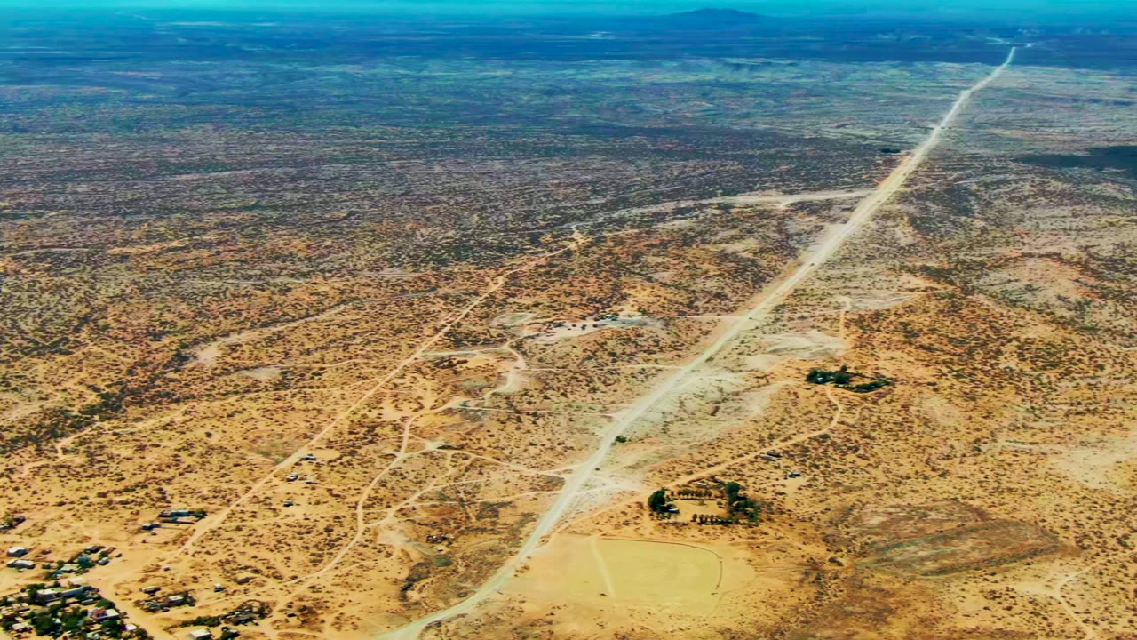 High aerial view in San Juanico, Baja California Sur with long straight dirt roads, scattered compounds, dry lots, and scrub-covered ground, with no visible people.