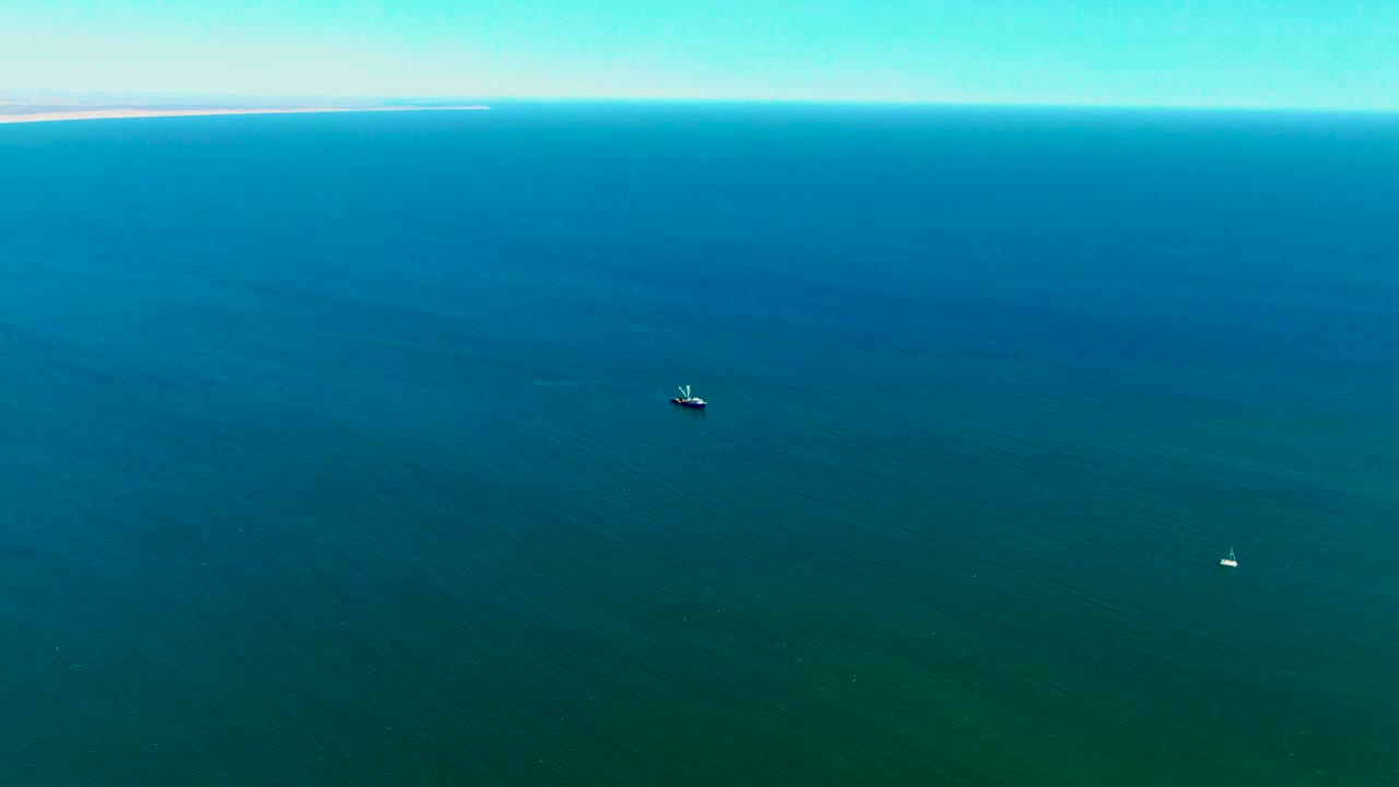 Aerial view near San Juanico, Baja California Sur showing a small boat on dark blue-green ocean water, a faint distant landmass along the upper edge, and no visible people.