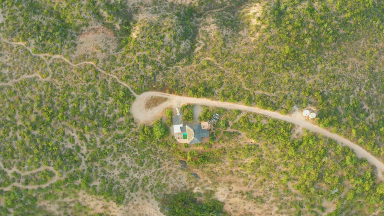 Overhead view of a small compound along a dusty road in scrub-covered terrain.