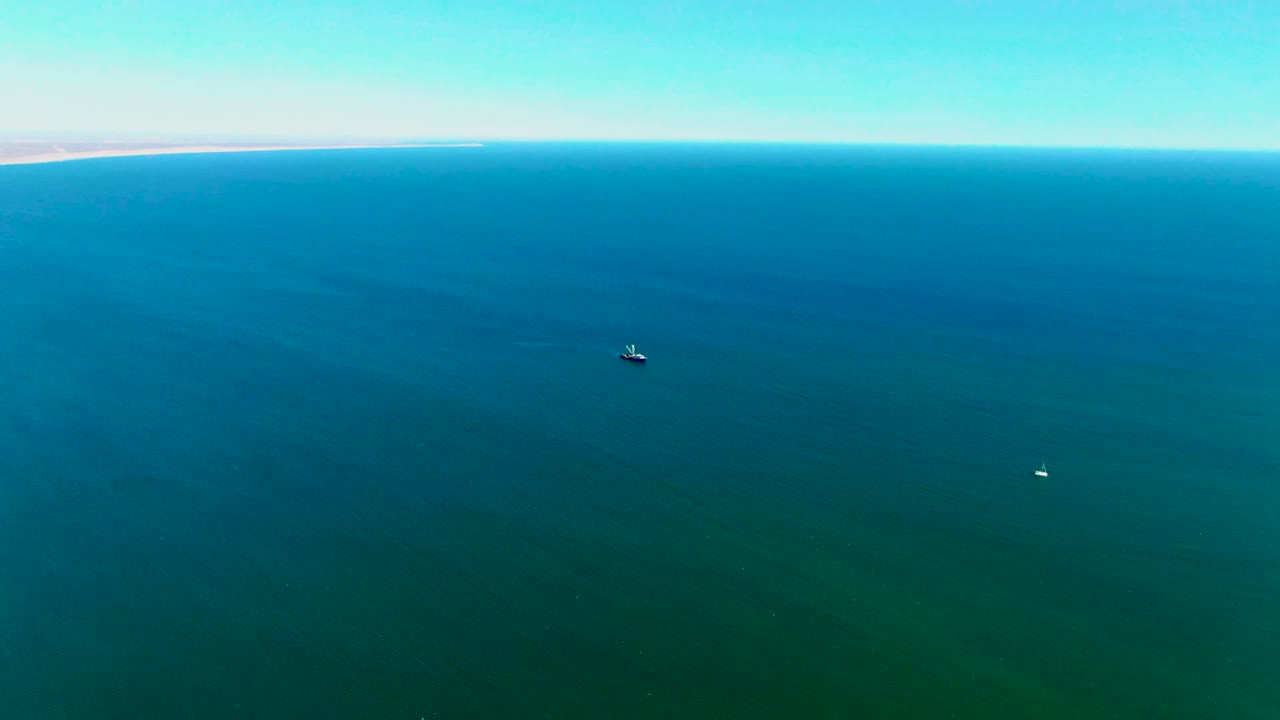 High aerial frame over San Juanico water with the small boat left of center, the buoy lower in the frame, thin shoreline on the horizon, and no visible people.