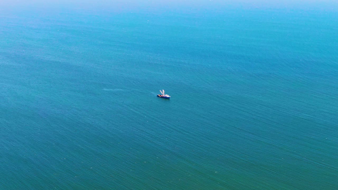 A wide aerial frame over San Juanico blue ocean water shows a small boat left of center with no visible people.