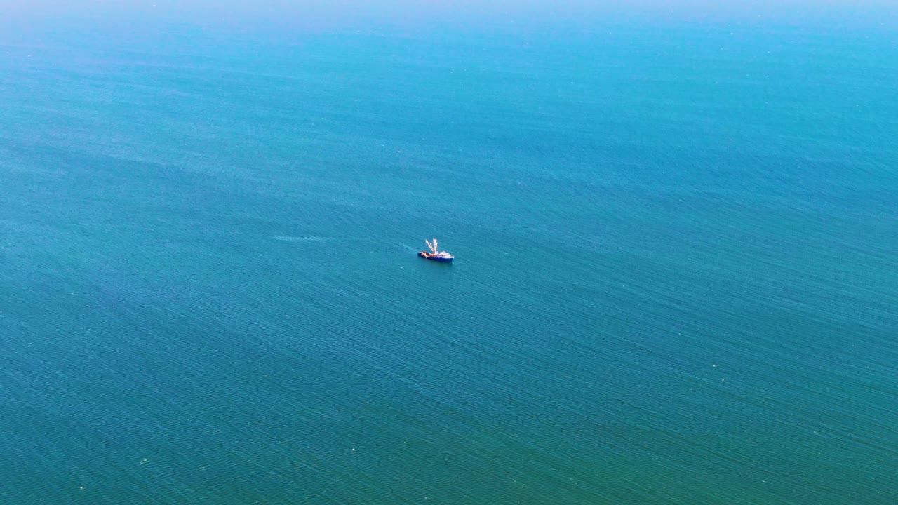 A San Juanico aerial frame shows the small boat slightly right of center over textured blue ocean, with no visible people or shoreline detail.