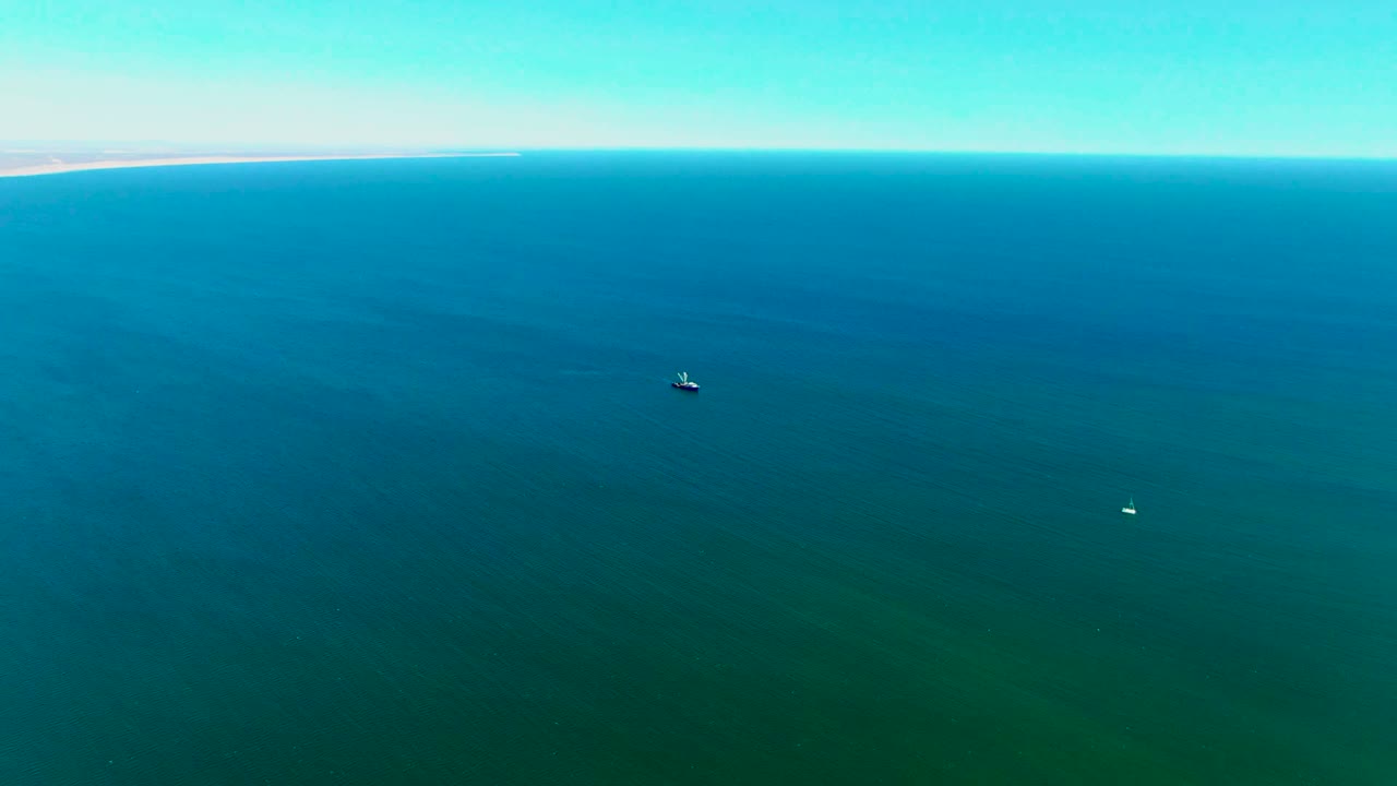 Aerial view over San Juanico ocean water with a pale distant shoreline near the horizon, two small boats separated across the frame, and no visible people.
