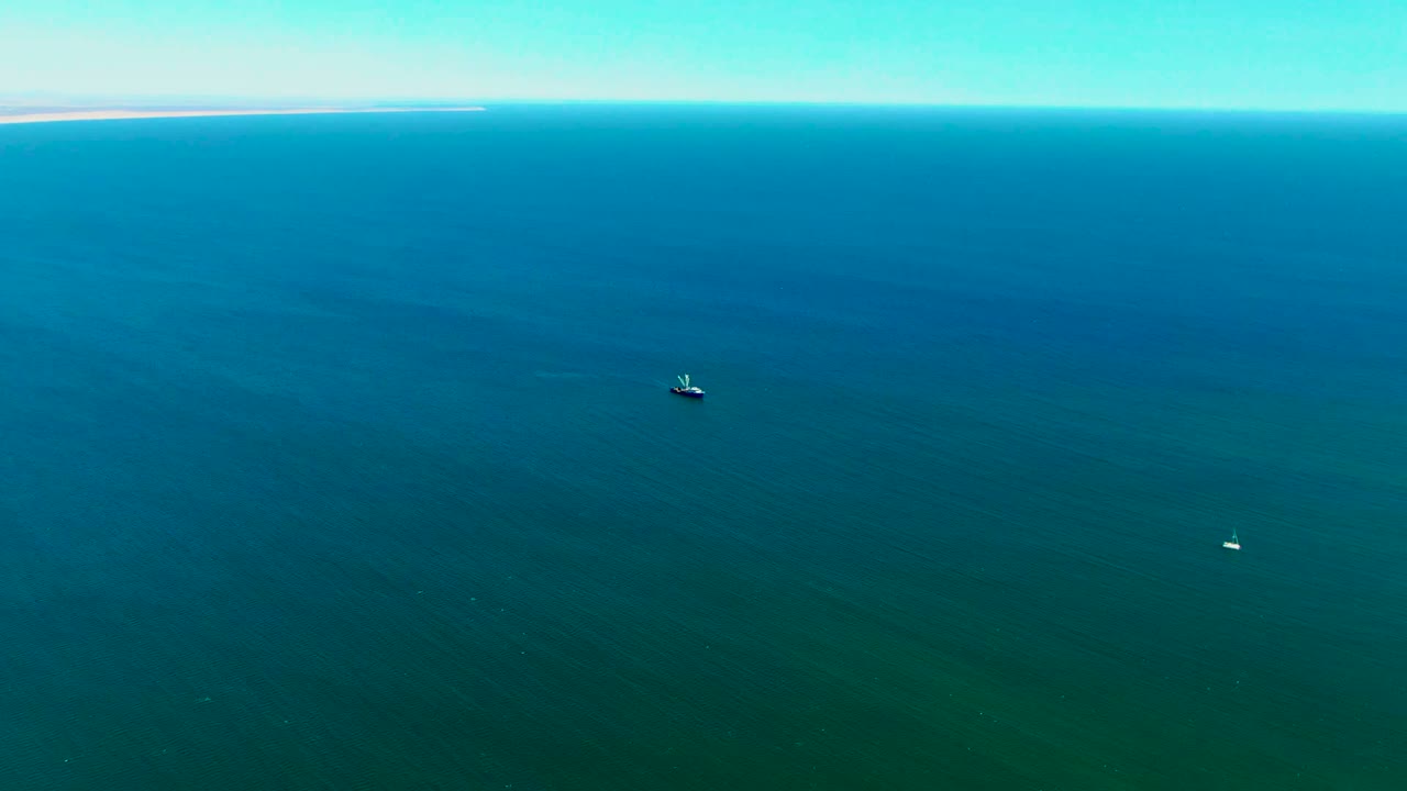 High view of San Juanico ocean with a small boat near the upper middle, a tiny white boat far to the right, soft surface bands, and no visible people.