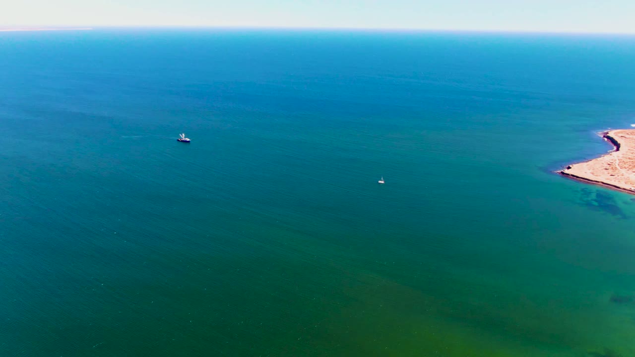Aerial ocean view with a small boat and sandy coastline entering at right.