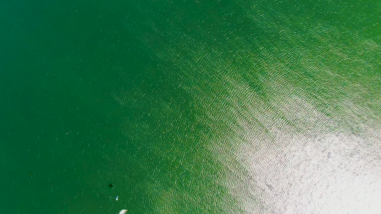 Aerial view of green rippled water off San Juanico, Baja California Sur, with a broad white sun reflection and tiny bright marks on the water surface, no visible people.