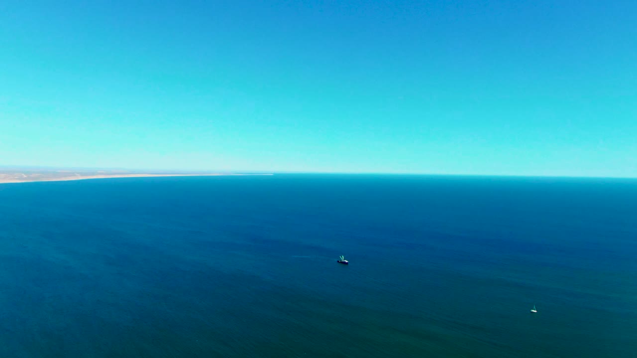 Blue ocean and clear sky with a low shoreline at the left horizon and a small dark object on the water.