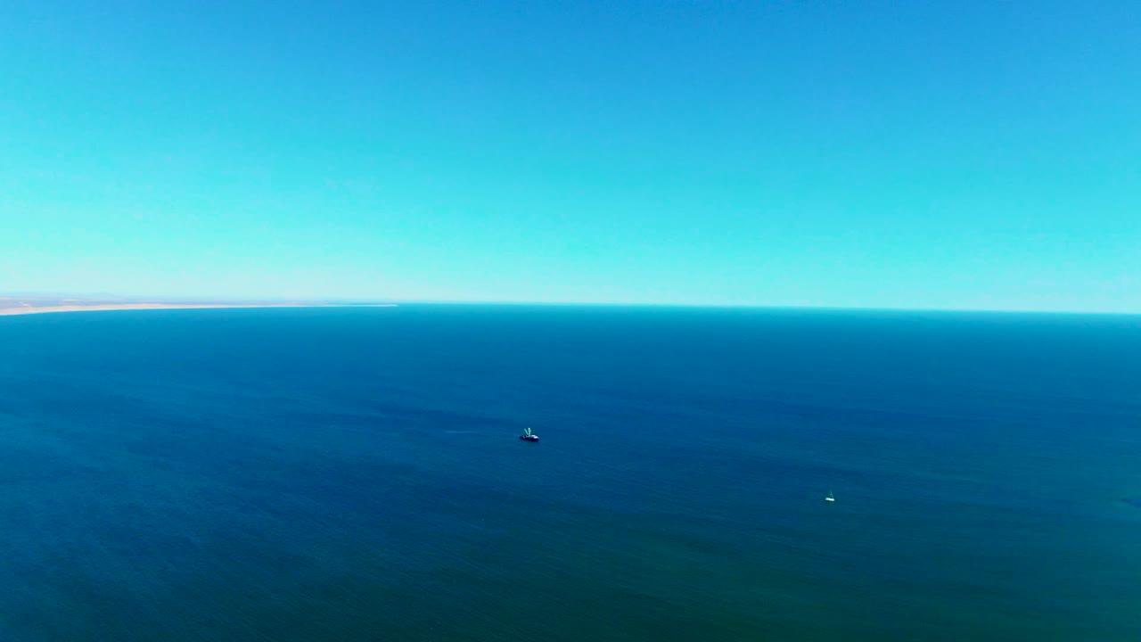Open blue ocean with a small boat below the horizon and distant shore on the left.