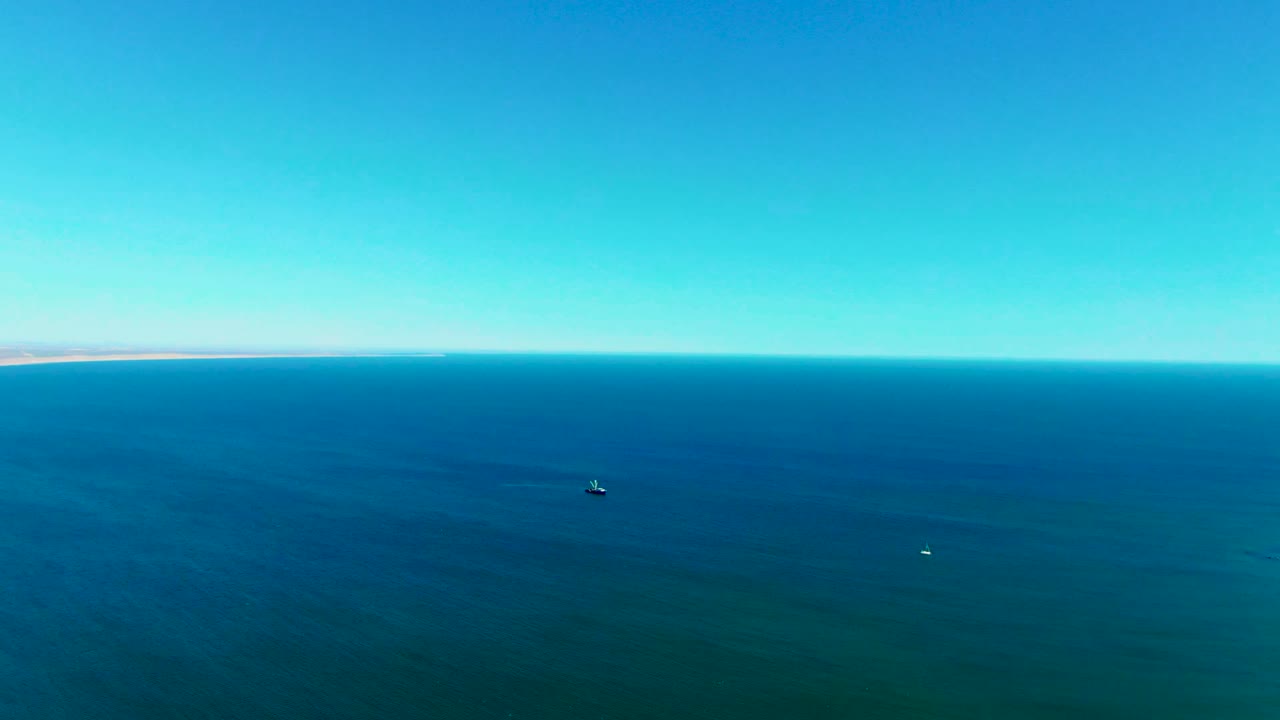 Open blue sea near San Juanico fills the frame beneath a clear sky, with small boats spaced across the water and no visible people.