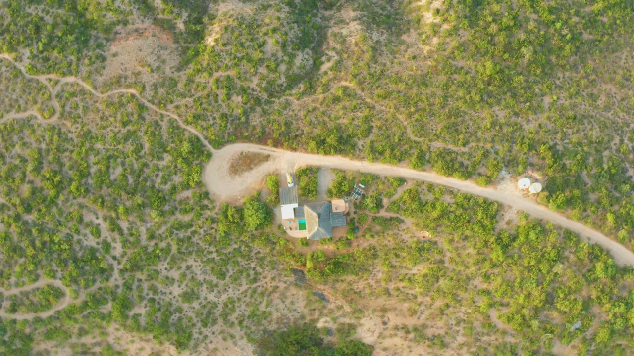 Rural compound and looping dirt road surrounded by green and dry brush.