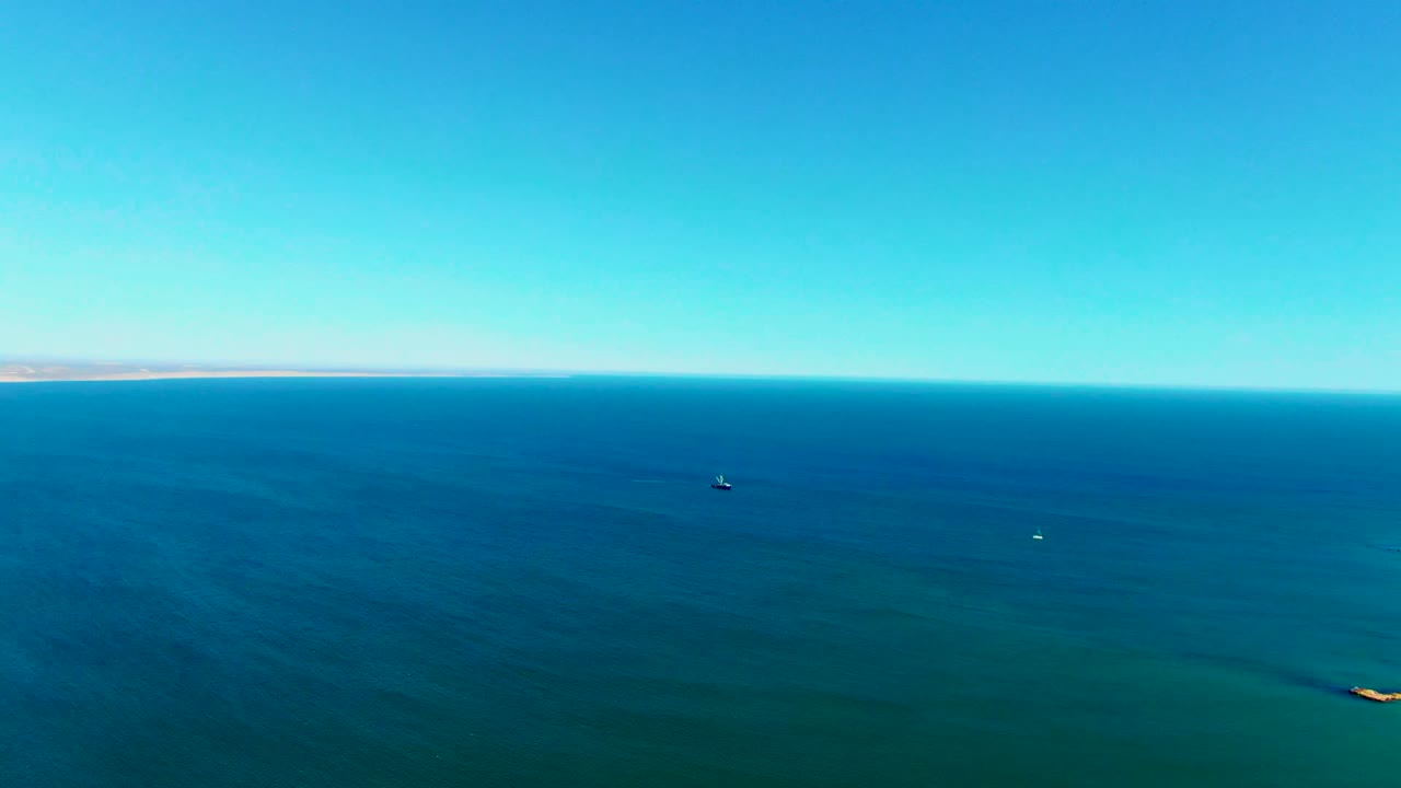 Open blue sea with a distant coast and a small vessel in the midground.