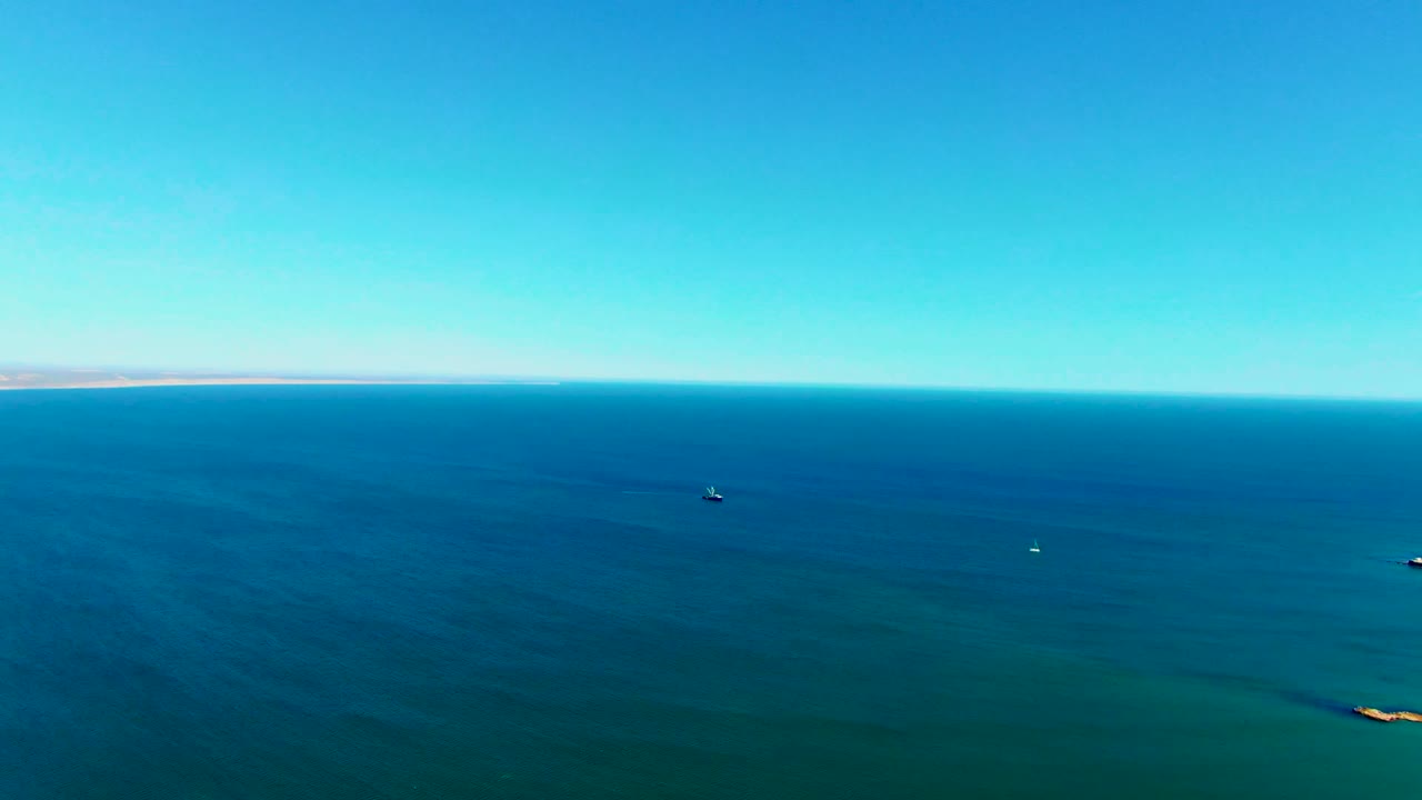 The San Juanico coastal view remains wide, with calm blue water, a far shoreline, small boats or buoys, and no visible people in frame.