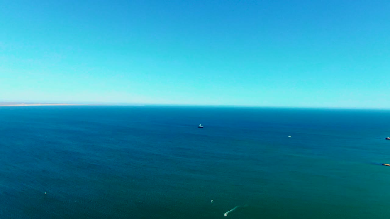 Aerial ocean view with a small boat near center and faint wake lines below.