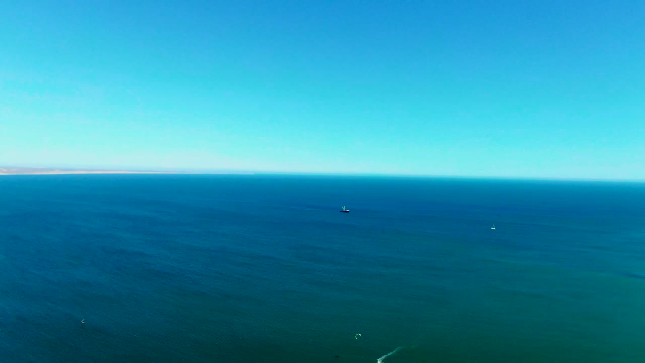 High aerial frame of blue ocean off San Juanico with scattered small boats near the horizon, green water in the foreground, and no visible people.