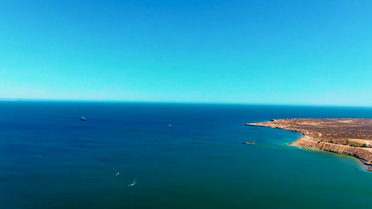 Aerial view over the San Juanico coast in Baja California Sur, Mexico, with turquoise water, clear sky, a distant boat near the horizon, and no visible people.