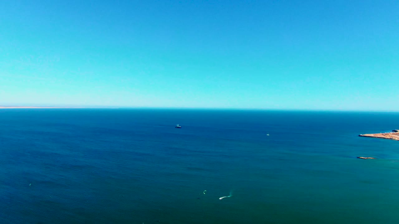 San Juanico aerial view with mostly open ocean, a small coastline sliver at the far right, distant dark boats near the horizon, pale wake marks, and no visible people.