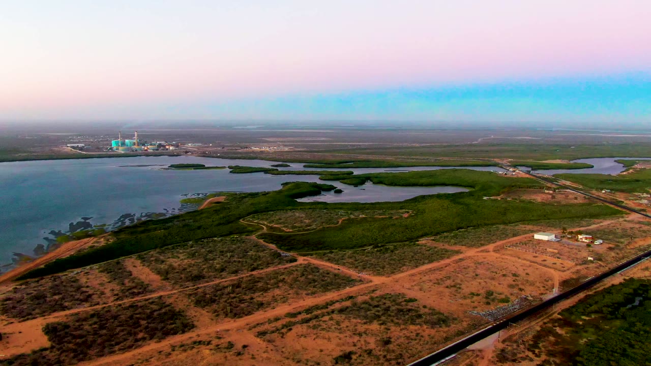 San Carlos, Baja California Sur aerial frame showing water along the left edge, green wetland patches across the middle, reddish dirt roadways below, and no visible people.