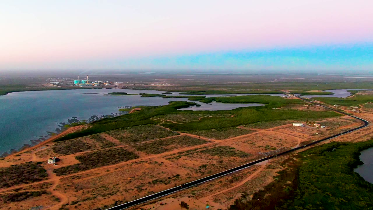 Wide aerial view of coastal wetlands, dirt roads, and a railway beside water.