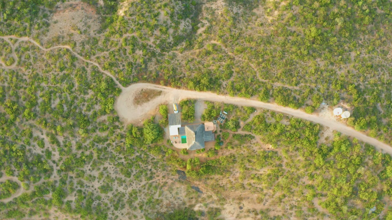 Aerial view of a car near rural buildings beside a winding dirt road.