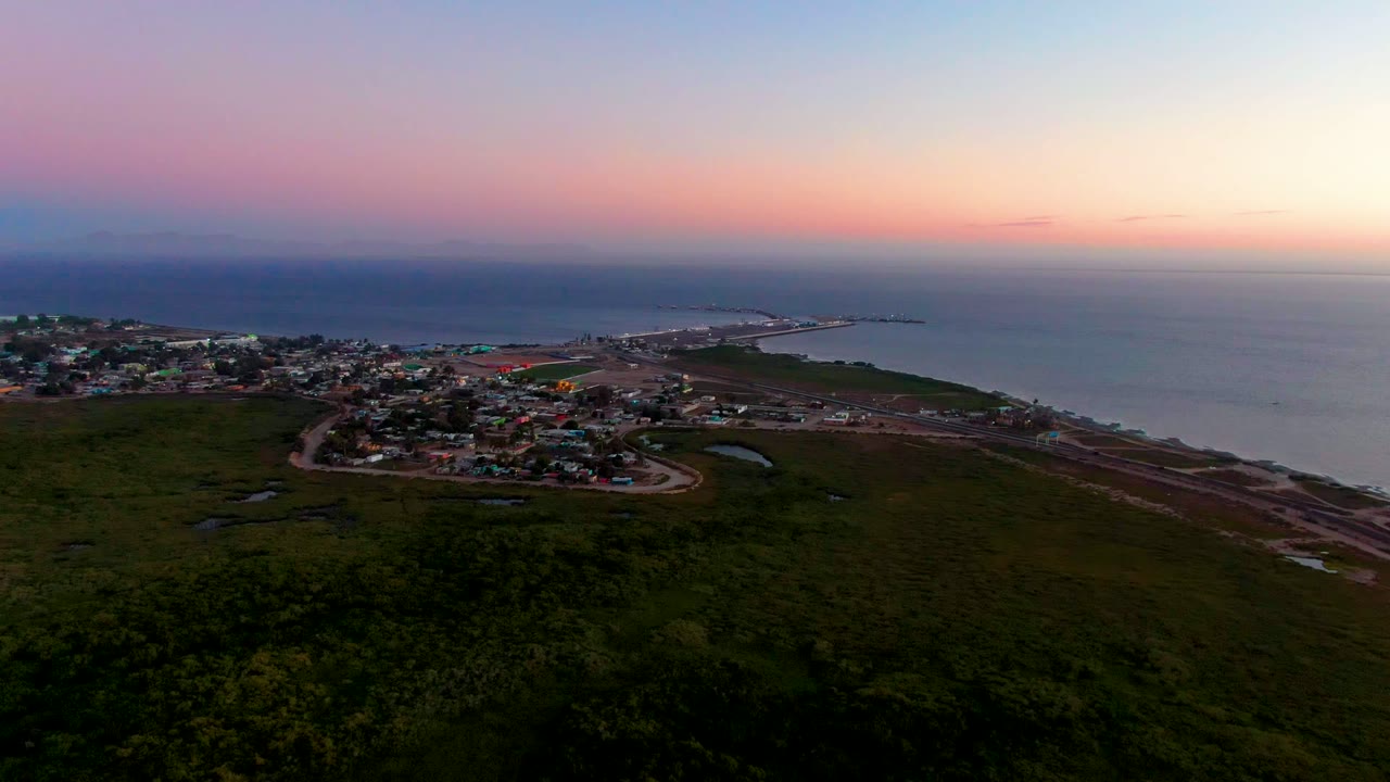 Coastal town and shoreline road under a pink dusk sky