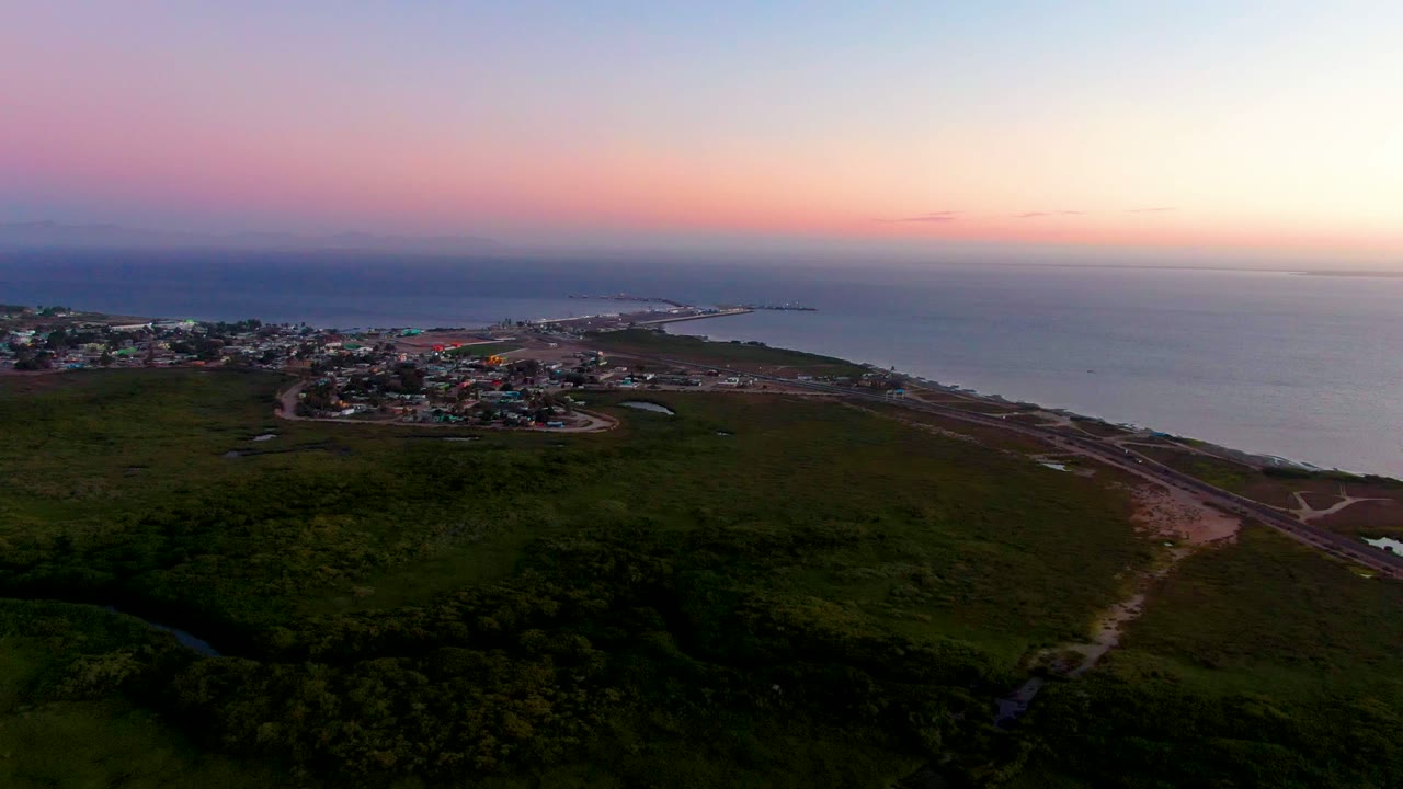 Coastal village and shoreline seen from above under a pink and purple sky.