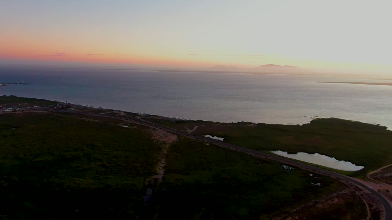 Coastal road and reflective pond with ocean horizon at dusk.
