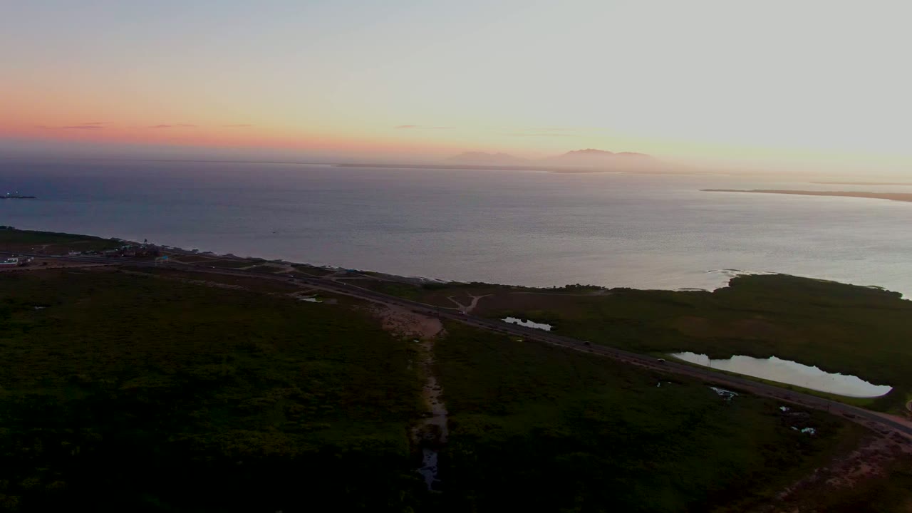 Coastal aerial with road and lagoon in foreground and ocean under dusk sky.