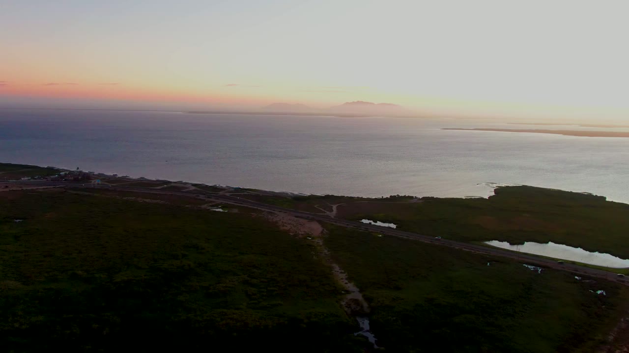 Coastal road and green fields below the ocean horizon at dusk.