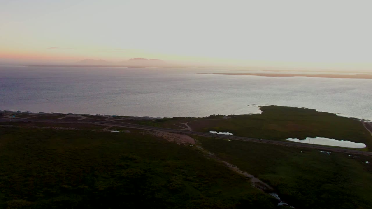 Wide aerial coast with road, ponds, and dusk ocean horizon.