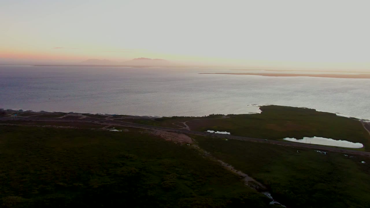 Aerial view in San Carlos, Baja California Sur, showing the coastline at dusk, a pale path across dark ground, bright pools beside it, a distant shoreline, and no visible people.