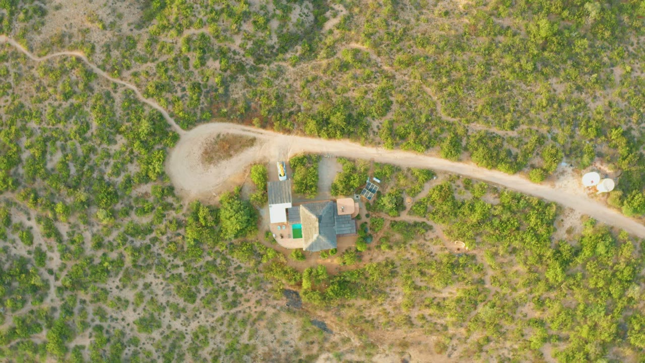 Overhead drone frame in Cabo Pulmo, Baja California Sur showing a rural house, a pale dirt road, surrounding green scrub, and no visible people at the start of the clip.