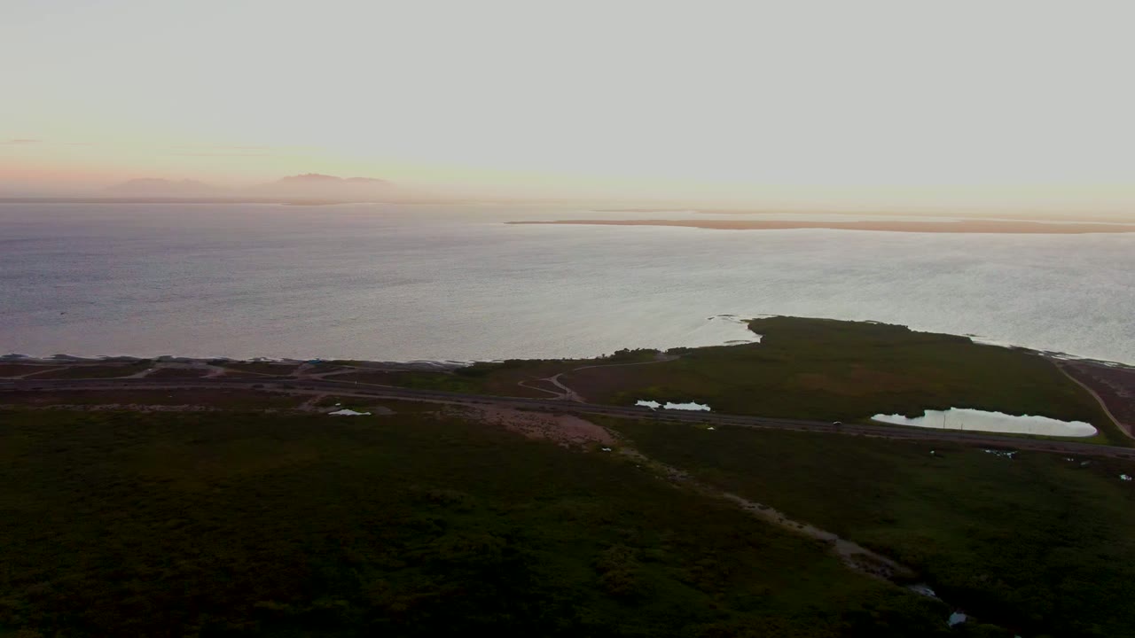 Elevated view of calm coastal water beyond a green headland and road at dusk.