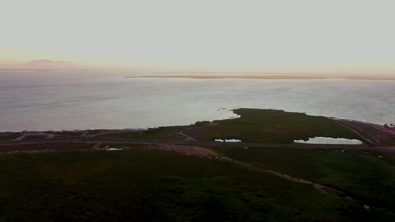 Wide wetland shoreline with ponds and pale sunset water