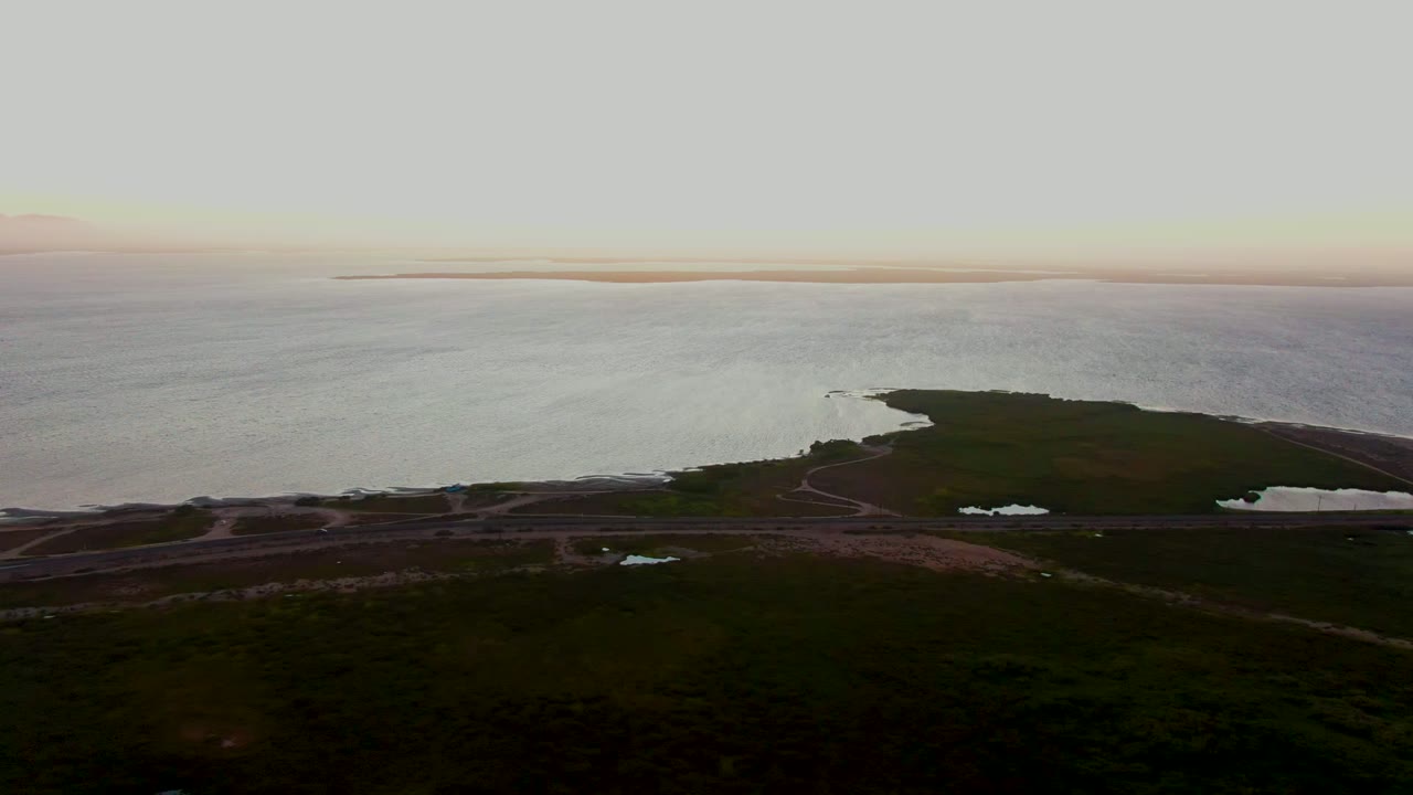 Drone view of a coastal point with water, road lines, and dark green terrain.