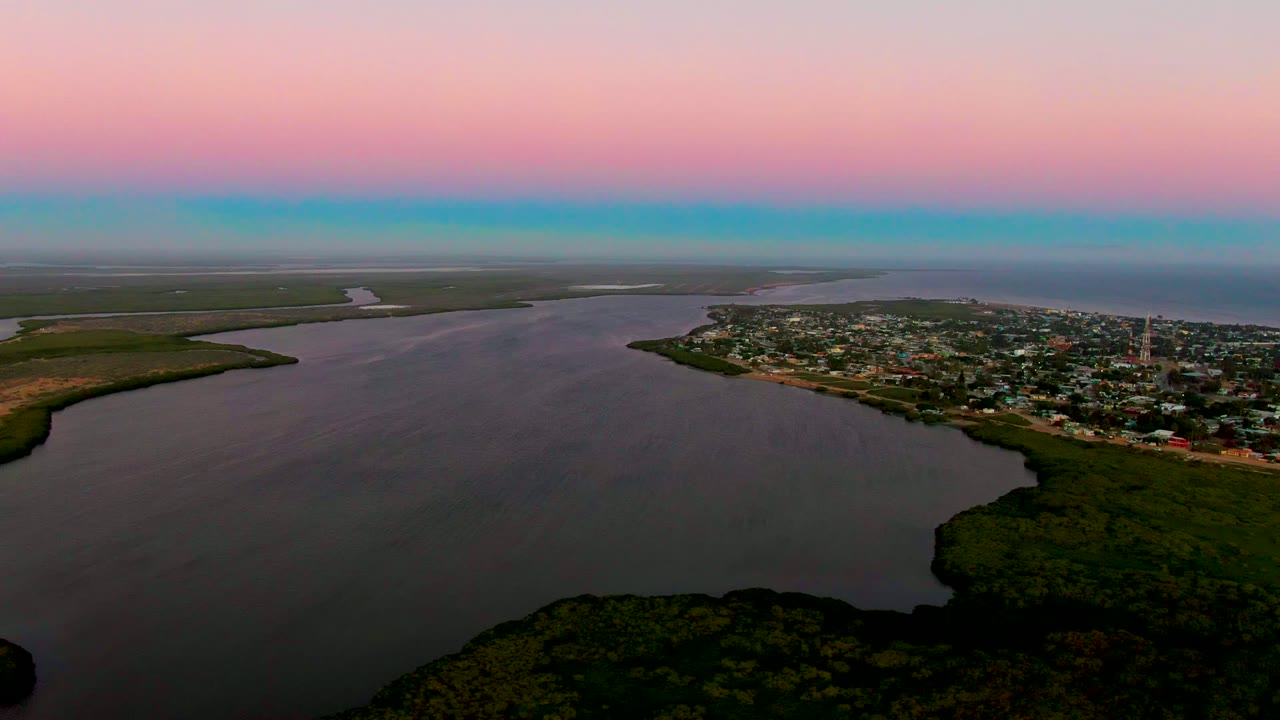 Wide aerial view of waterway beside a town under pink dusk sky.