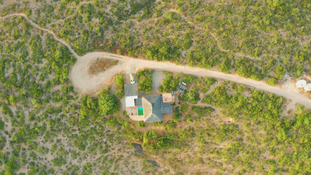 Aerial view of dirt road, compound, brush, and white objects near the road