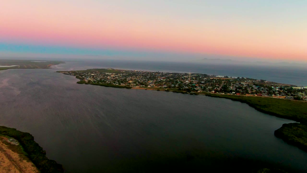 San Carlos appears as a low band of town blocks and shoreline greenery between the lagoon foreground and the darker ocean horizon, with no visible people.