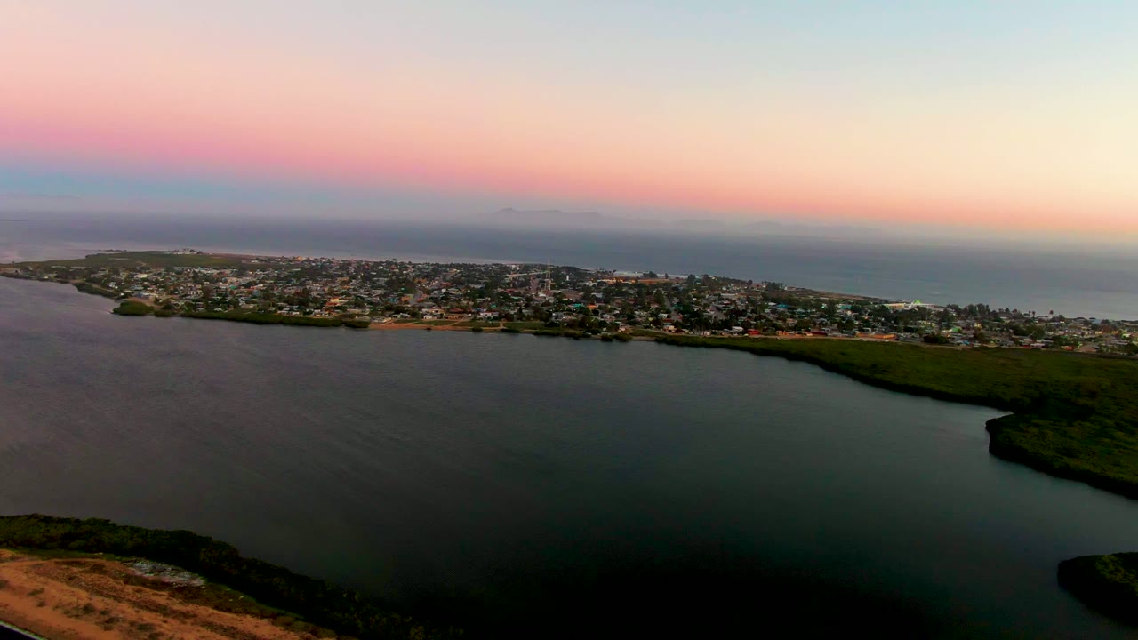 Wide drone view over calm bay water toward a coastal town at dusk.