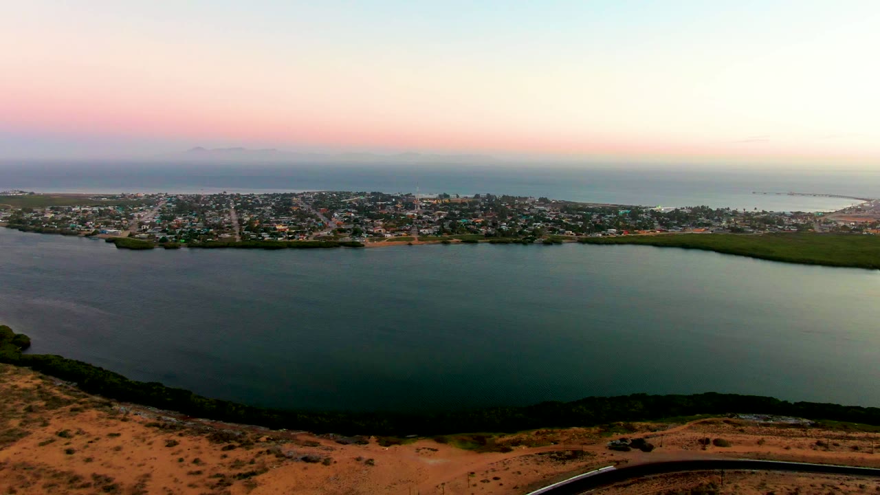 Calm bay below a coastal town with dry terrain in front.